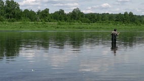 Fiskarefiske i en lugna flod i morgonen Man i fiskekugghjulet som stending i en flod och kast en fiskepol stock video Fiskarefiske i en lugna flod i morgonen Man i fiskekugghjulet som stending i en flod och kast en fiskepol stock video