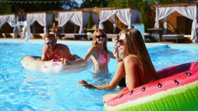 Fitted friends have pool party dancing with inflatable mattress, watermelon floaty toys. Attractive hot pretty glamour