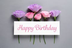Flat lay composition of Eustoma flowers and card with greeting HAPPY BIRTHDAY