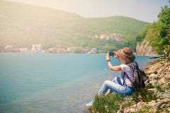 Flickahandelsresanden sitter på en bergsjö och tar bilder som flickan tar fotoet för loppblogg Sikt från baksida av den turist- h arkivbild Flickahandelsresanden sitter på en bergsjö och tar bilder som flickan tar fotoet för loppblogg Sikt från baksida av den turist- h arkivbild