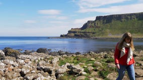 Flickaklättringar över vaggar på jättevägbanken i nordligt - Irland lager videofilmer Flickaklättringar över vaggar på jättevägbanken i nordligt - Irland lager videofilmer