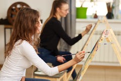Flickan med den bruna ikl?dda vita blusen f?r lockigt h?r m?lar en bild p? staffli i den dra skolan arkivfoton Flickan med den bruna ikl?dda vita blusen f?r lockigt h?r m?lar en bild p? staffli i den dra skolan arkivfoton
