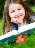 Flickan med äpplet läser boken som ligger på det gröna gräset royaltyfri bild Flickan med äpplet läser boken som ligger på det gröna gräset royaltyfri bild