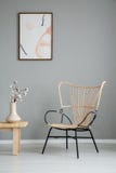 Flowers on wooden table next to modern armchair in grey apartment interior with poster. Real photo stock image Flowers on wooden table next to modern armchair in grey apartment interior with poster. Real photo stock image