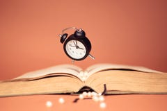 Flying clock and book on orange background. stock photo Flying clock and book on orange background. stock photo