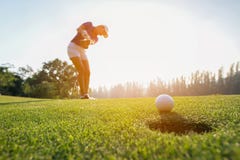 Foco asiático da mulher do jogador de golfe que põe a bola de golfe sobre o golfe verde em tempo ajustado da noite do sol fotos de stock royalty free Foco asiático da mulher do jogador de golfe que põe a bola de golfe sobre o golfe verde em tempo ajustado da noite do sol fotos de stock royalty free