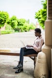 Focused young Afro american female college student looking deep in thought while sitting on a bench working on a laptop on campus stock photos Focused young Afro american female college student looking deep in thought while sitting on a bench working on a laptop on campus stock photos