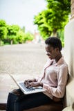 Focused young Afro american female college student looking deep in thought while sitting on a bench working on a laptop on campus stock images Focused young Afro american female college student looking deep in thought while sitting on a bench working on a laptop on campus stock images