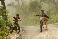 Foggy morning of a village road surrounded by firm land and two little boys cycling blurry due to motion, selective focus. 8th April, 2022, Kalimpong, West