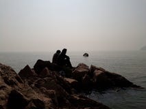 Folket som sitter och tycker om att sitta på, vaggar på havsstranden arkivfoto Folket som sitter och tycker om att sitta på, vaggar på havsstranden arkivfoto
