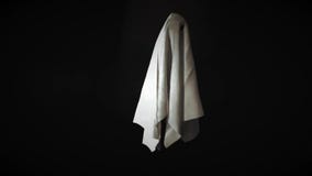Footage of ghost white sheet costume flying in the air with black background.