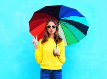 Forme a la mujer bastante fresca que sostiene el paraguas colorido en día del otoño sobre el fondo azul que lleva un suéter hecho Fotografía de archivo libre de regalías Forme a la mujer bastante fresca que sostiene el paraguas colorido en día del otoño sobre el fondo azul que lleva un suéter hecho Fotografía de archivo libre de regalías
