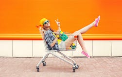 Forme a menina consideravelmente fresca no carro do trole que tem o divertimento sobre a laranja colorida Fotos de Stock Forme a menina consideravelmente fresca no carro do trole que tem o divertimento sobre a laranja colorida Fotos de Stock