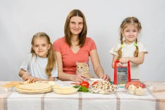 Fostra och två små flickor på förberedda ingredienser för tabellen för pizza De höll ögonen på en katt fotografering för bildbyråer Fostra och två små flickor på förberedda ingredienser för tabellen för pizza De höll ögonen på en katt fotografering för bildbyråer