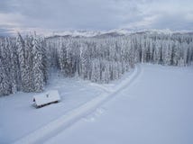 Foto aérea de uma casa de madeira ao lado da floresta e montanhas cobertas na neve atrás dela no inverno frio fotos de stock Foto aérea de uma casa de madeira ao lado da floresta e montanhas cobertas na neve atrás dela no inverno frio fotos de stock