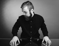 Foto in bianco e nero di un uomo con una barba e una pettinatura alla moda vestite nella camicia nera che controlla lo specchio c immagini stock libere da diritti Foto in bianco e nero di un uomo con una barba e una pettinatura alla moda vestite nella camicia nera che controlla lo specchio c immagini stock libere da diritti
