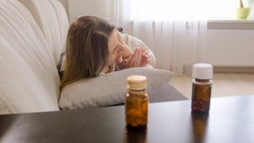 Foto delle pillole sul comodino accanto alla donna malata che si trova sul sofà Fotografie Stock Foto delle pillole sul comodino accanto alla donna malata che si trova sul sofà Fotografie Stock