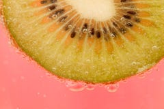 Foto macro da fatia do fruto de quivi com bolhas na água com fundo cor-de-rosa foto de stock royalty free Foto macro da fatia do fruto de quivi com bolhas na água com fundo cor-de-rosa foto de stock royalty free