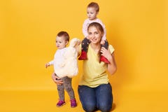 Foto van gelukkige familie Het mamma met haar tweelingenmeisjes die in studio stellen, mum houdt één jong geitje op schouders, ge stock fotografie Foto van gelukkige familie Het mamma met haar tweelingenmeisjes die in studio stellen, mum houdt één jong geitje op schouders, ge stock fotografie