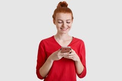 Fotoet av den tillfredsställda röda haired kvinnan med fräknig hud, rymmer den moderna mobiltelefonen, överför textmeddelandet, a royaltyfri foto Fotoet av den tillfredsställda röda haired kvinnan med fräknig hud, rymmer den moderna mobiltelefonen, överför textmeddelandet, a royaltyfri foto