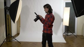 Fotógrafo que senta-se em seu estúdio da foto que verifica as fotografias de sua câmara digital e que estão sendo satisfeitas de vídeos de arquivo Fotógrafo que senta-se em seu estúdio da foto que verifica as fotografias de sua câmara digital e que estão sendo satisfeitas de vídeos de arquivo