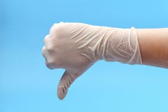 Fragment d'une main dans les gants médicaux blancs que les expositions manient maladroitement vers le bas sur un fond bleu Pouce photos stock Fragment d'une main dans les gants médicaux blancs que les expositions manient maladroitement vers le bas sur un fond bleu Pouce photos stock