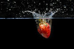 Fragola che cade nell'acqua e che spruzza le gocce sulla b nera fotografia stock libera da diritti Fragola che cade nell'acqua e che spruzza le gocce sulla b nera fotografia stock libera da diritti