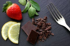 Fragole, fette del limone, foglie di menta, forcella d'argento e cioccolato nero sul fondo nero dell'ardesia fotografie stock libere da diritti Fragole, fette del limone, foglie di menta, forcella d'argento e cioccolato nero sul fondo nero dell'ardesia fotografie stock libere da diritti