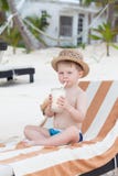 Frappè sorseggiante del bambino sveglio sulla spiaggia fotografia stock Frappè sorseggiante del bambino sveglio sulla spiaggia fotografia stock