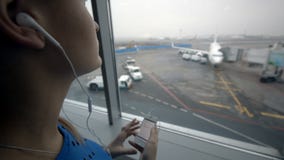 Frau, die am Fenster Musik am Flughafen hört stock footage Frau, die am Fenster Musik am Flughafen hört stock footage