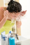 Frau, die Wasser auf Gesicht im Badezimmer spritzt Lizenzfreie Stockbilder Frau, die Wasser auf Gesicht im Badezimmer spritzt Lizenzfreie Stockbilder