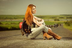 Frau mit der Gitarre, die am Asphalt sitzt stockfotografie Frau mit der Gitarre, die am Asphalt sitzt stockfotografie