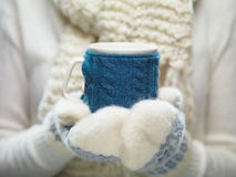 Frauenhände in den weißen und blauen Handschuhen, die eine gemütliche gestrickte Schale mit heißem Kakao, Tee oder Kaffee halten Lizenzfreie Stockbilder Frauenhände in den weißen und blauen Handschuhen, die eine gemütliche gestrickte Schale mit heißem Kakao, Tee oder Kaffee halten Lizenzfreie Stockbilder