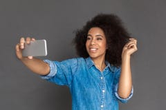 Freestyle. Mulatto woman standing isolated on grey taking selfie on smartphone smiling happy royalty free stock photography Freestyle. Mulatto woman standing isolated on grey taking selfie on smartphone smiling happy royalty free stock photography