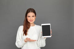 Freestyle. Young girl standing on grey showing screen of digital tablet smiling friendly stock photos Freestyle. Young girl standing on grey showing screen of digital tablet smiling friendly stock photos