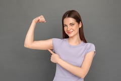 Freestyle. Young girl standing isolated on grey showing arm muscle smiling confident close-up stock photo Freestyle. Young girl standing isolated on grey showing arm muscle smiling confident close-up stock photo