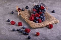 Fresh blueberries and raspberries scattered from a transparent bucket on a gray concrete stock photography Fresh blueberries and raspberries scattered from a transparent bucket on a gray concrete stock photography
