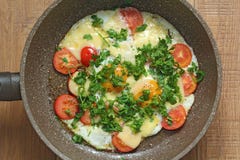 Fresh fried eggs are cooked in a frying pan, with tomatoes, cheese and greens. Vegetarian dishes. Bright healthy food on a wooden stock photography Fresh fried eggs are cooked in a frying pan, with tomatoes, cheese and greens. Vegetarian dishes. Bright healthy food on a wooden stock photography