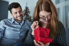 Freundin schaut zu ihrem Weihnachtsgeschenk skeptisch lizenzfreie stockfotografie Freundin schaut zu ihrem Weihnachtsgeschenk skeptisch lizenzfreie stockfotografie
