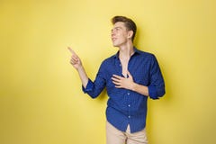 Friendly looking cheerful european guy with dark hair wearing blue shirt, smiling widely, pointing left while standing royalty free stock images Friendly looking cheerful european guy with dark hair wearing blue shirt, smiling widely, pointing left while standing royalty free stock images