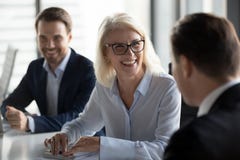 Friendly middle aged female leader laughing at group business meeting