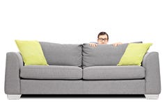 Frightened man hiding behind a sofa stock image Frightened man hiding behind a sofa stock image