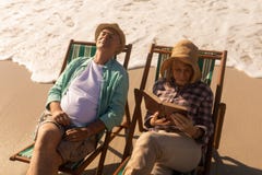 Senior woman reading a book while senior man relaxing on sun lounger at beach royalty free stock photo Senior woman reading a book while senior man relaxing on sun lounger at beach royalty free stock photo