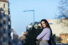 Front view of smiling beautiful young woman hand on pocket, touching hair and standing in the street while looking away in a sunny stock photo Front view of smiling beautiful young woman hand on pocket, touching hair and standing in the street while looking away in a sunny stock photo