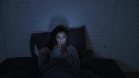 Frontal shot of young attractive hispanic woman on her 30s lying in bed late night using mobile phone look