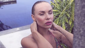 Fronte vicino su della donna bionda sexy in bikini che prende all'aperto doccia alla piscina circondata con il giardino tropicale archivi video Fronte vicino su della donna bionda sexy in bikini che prende all'aperto doccia alla piscina circondata con il giardino tropicale archivi video