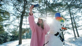 Fun selfie photo in winter forest backlit, cute girl making photo with a snowman, winter selfie, mobile phone in hand of stock video Fun selfie photo in winter forest backlit, cute girl making photo with a snowman, winter selfie, mobile phone in hand of stock video
