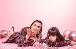 Funny mom and child lie on a pink background. Little girl and mother having fun with confetti royalty free stock images Funny mom and child lie on a pink background. Little girl and mother having fun with confetti royalty free stock images