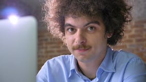 Funny nerd hacker typing on laptop and looking at camera smiling, brick wall background stock footage Funny nerd hacker typing on laptop and looking at camera smiling, brick wall background stock footage