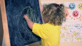 Funny 2 years old child girl drawing with chalk at blackboard